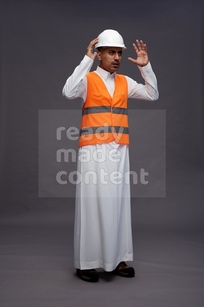 Saudi man wearing thob with engineer vest standing hands on head on gray background
