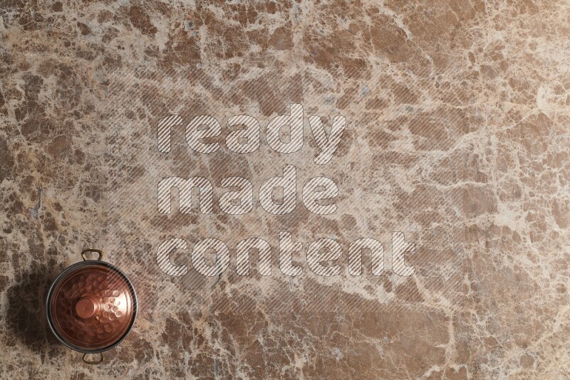 A small copper pot on beige marble background