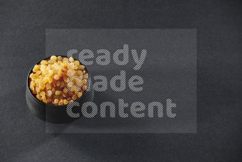 A black pottery bowl full of raisins on a black background in different angles