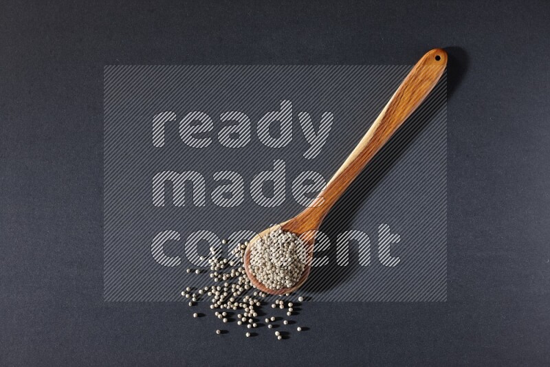 A wooden ladle full of white pepper beads on black flooring