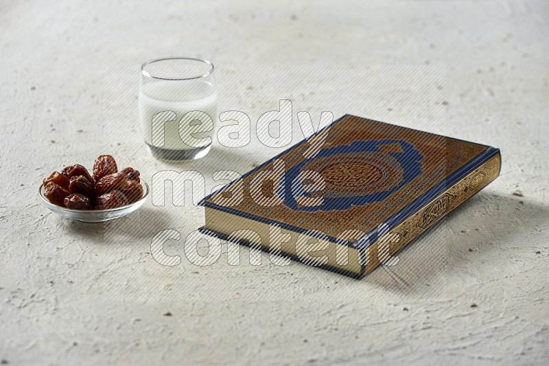 Quran with dates, prayer beads and different drinks all placed on textured white background