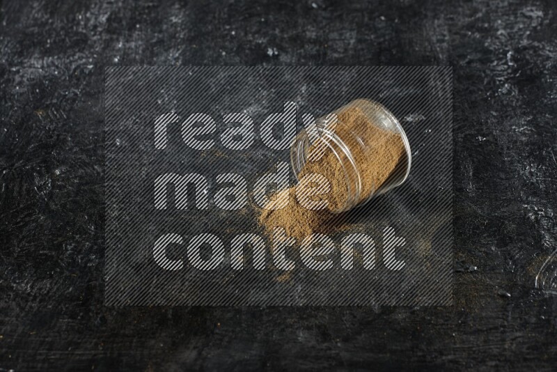 وعاء زجاجي مقلوب ممتلئ ببودرة الكمون والبودرة تناثرت منه على خلفية سوداء