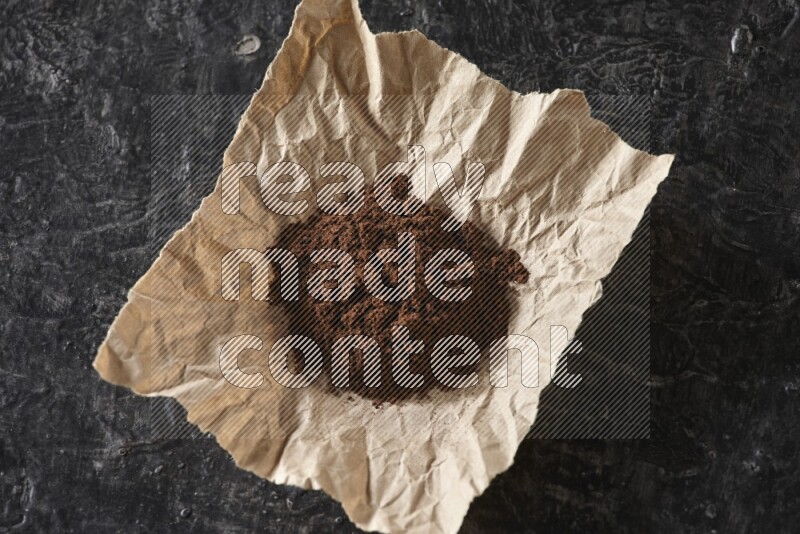 Cloves powder in crumpled piece of paper on a textured black flooring