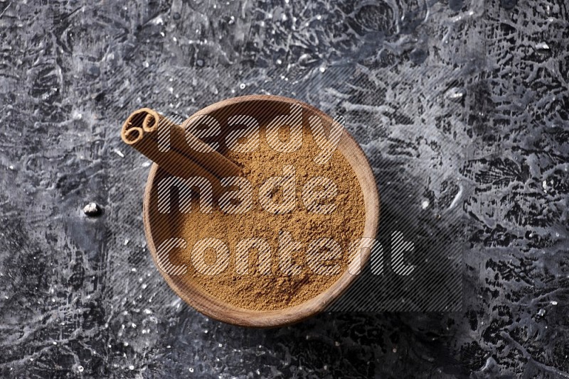 بودرة القرفة في وعاء خشبي مع عود من القرفة على خلفية سوداء