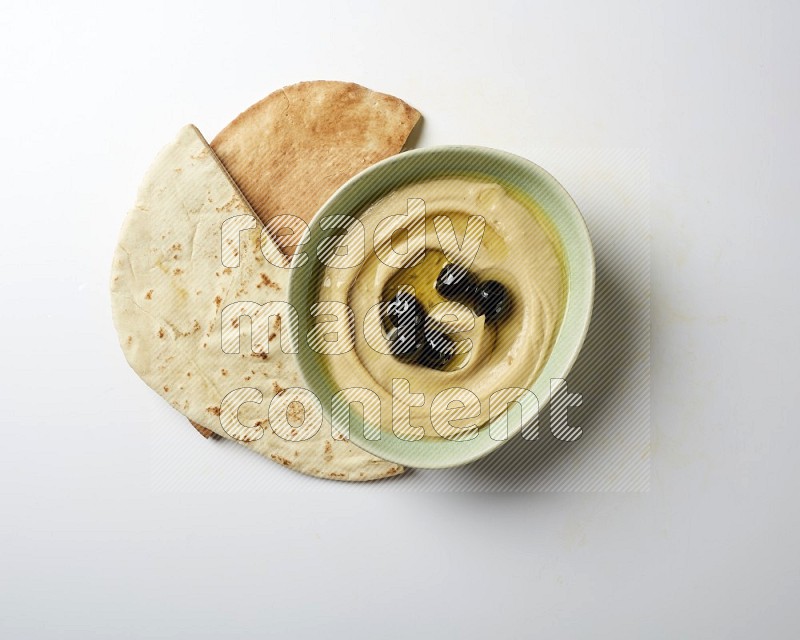 Hummus in a green plate garnished with black olives on a white background