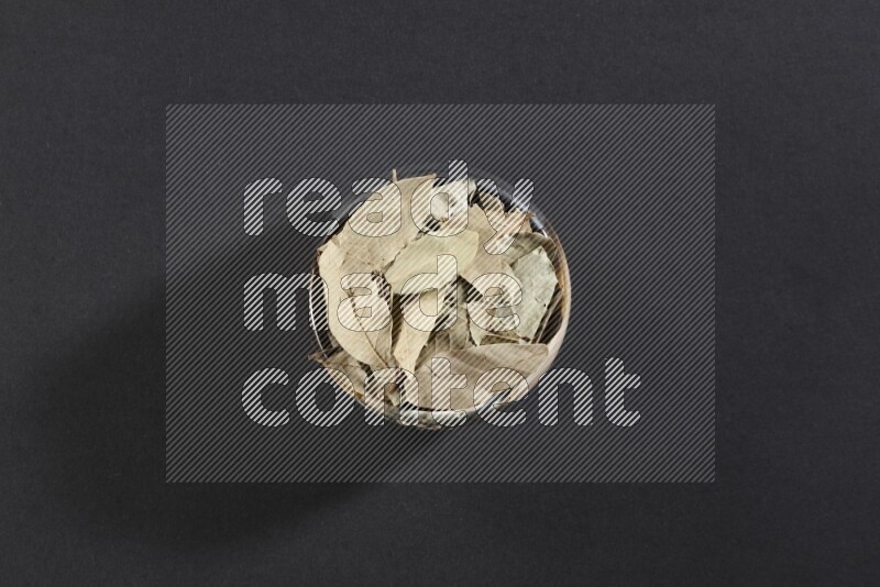 A multicolored pottery bowl full of dried bay leaves on black flooring
