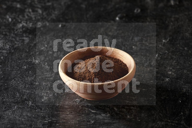 A wooden bowl full of cloves powder on a textured black flooring