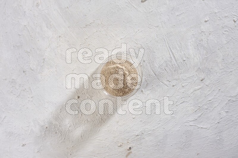 A glass jar full of garlic powder on a textured white flooring