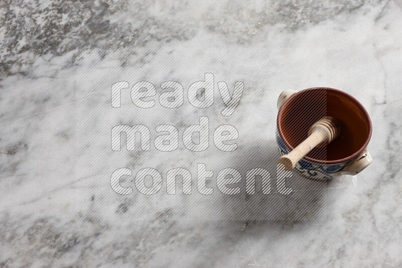 Decorative pottery pot with wooden honey dipper in it on grey marble background