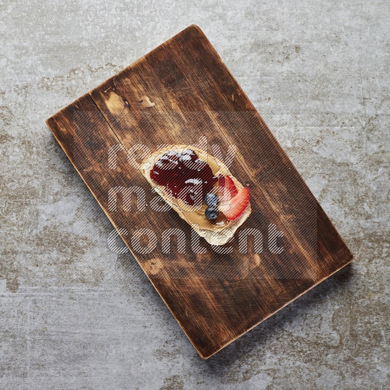 open faced peanut butter sandwich with jam, strawberries and blueberries & chia on a  grey textured background
