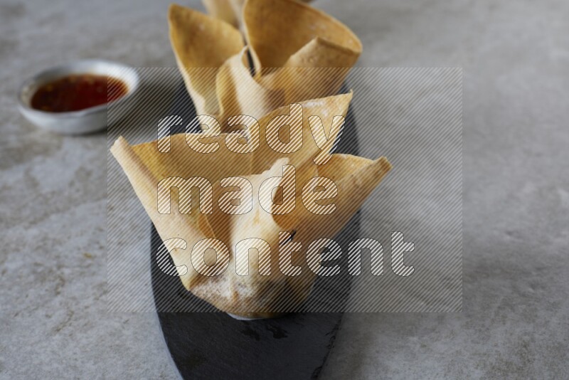 wonton cups with soy sauce ramkin on oval slate on grey textured counter top