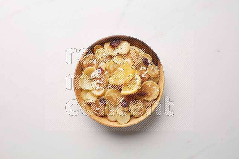 Top-view shot of orange candy cereal pancakes in a round bowl on white background