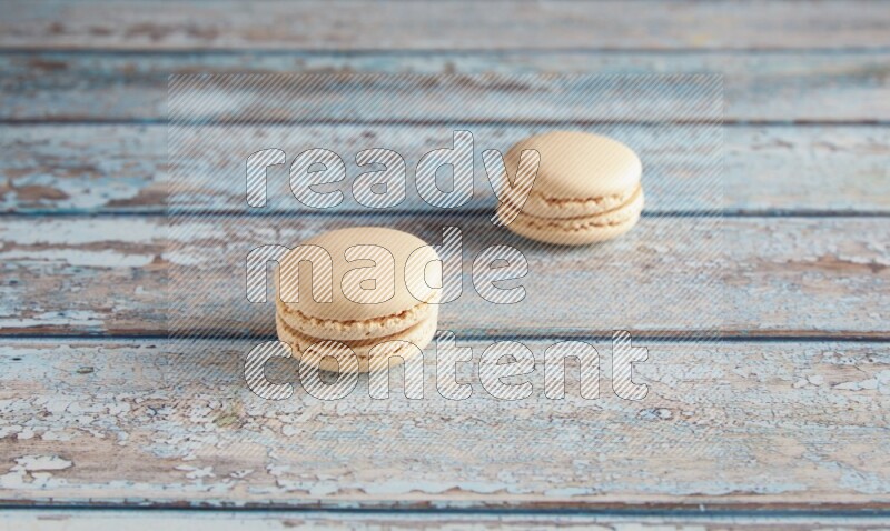 45º Shot of two White Caramel fleur de sel macarons on a light blue wooden background