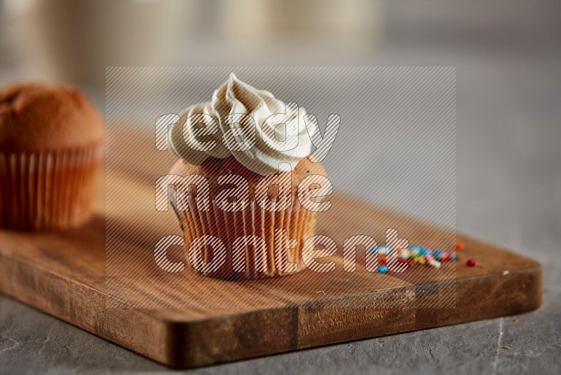 Vanilla cupcake topped with cream on a wooden board