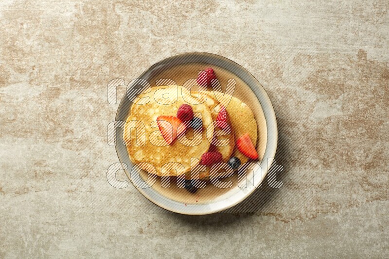 Three stacked mixed berries pancakes in a bicolor plate on beige background