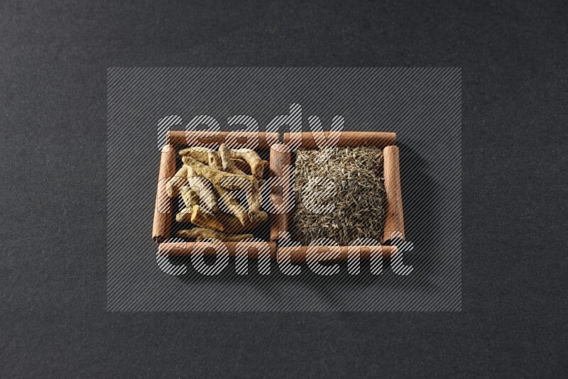 مربعان من أعواد القرفة ممتلئان بحبوب الكمون وأصابع الكركم علي خلفية سوداء