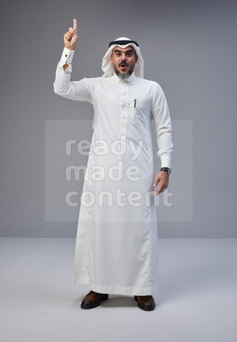 Saudi man Wearing Thob and white Shomag standing interacting with the camera on Gray background