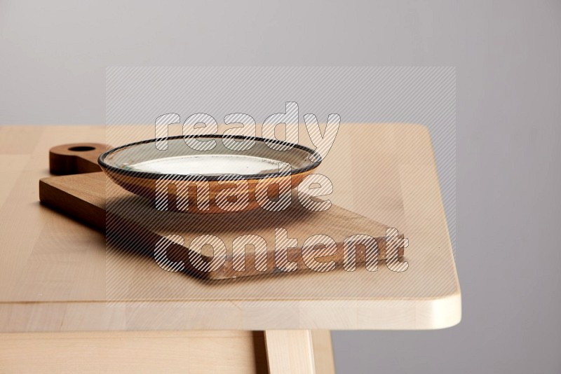 multi-colored pottery Plate placed on a  wooden rectangular cutting board on the edge of wooden table