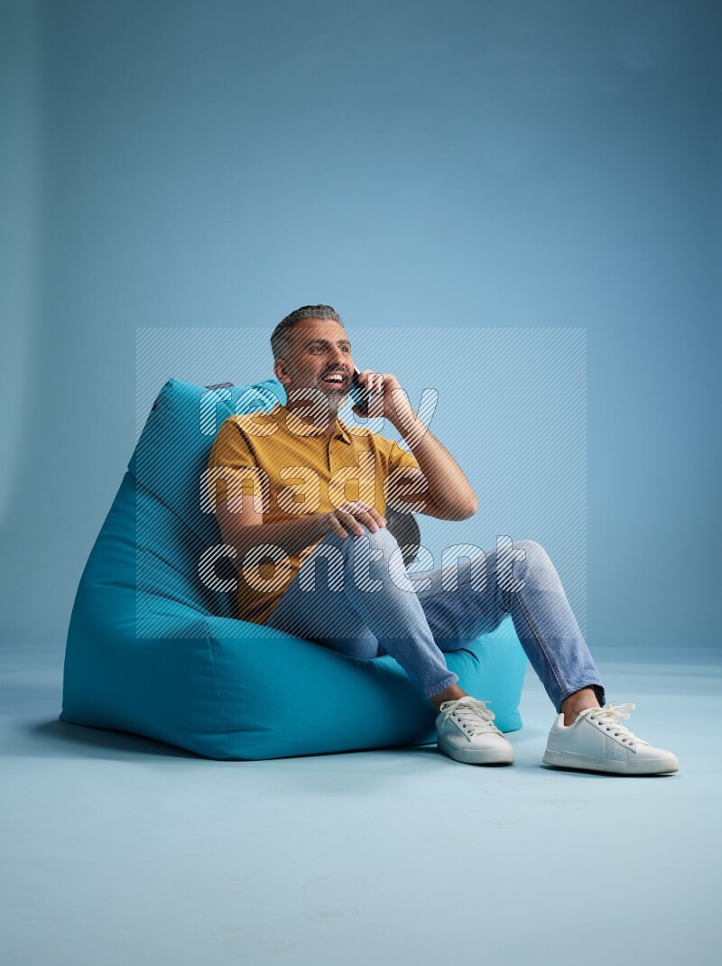 A man sitting on a blue beanbag and talking on the phone