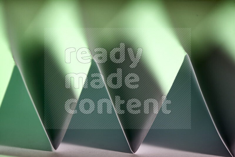 A close-up abstract image showing sharp geometric paper folds in green gradients
