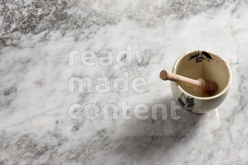 Decorative Pottery Bowl with wooden honey handle in it, on grey marble flooring, 65 degree angle