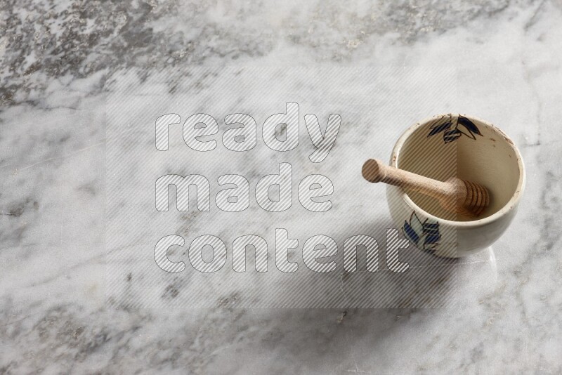 Decorative pottery bowl with wooden honey dipper in it on grey marble background