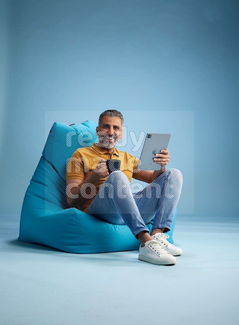 A man sitting on a blue beanbag and drinking coffee