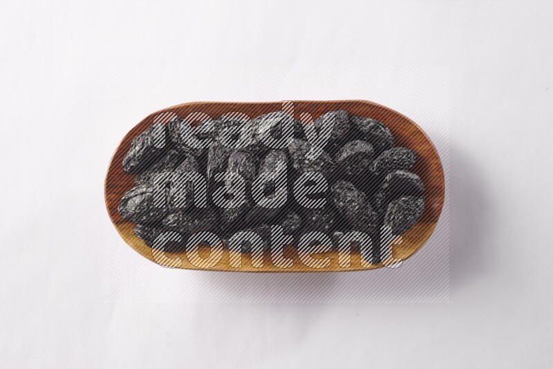 Dried plums in a wooden plate on white background