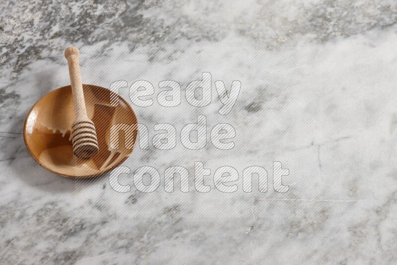 Multicolored pottery plate with wooden honey dipper in it on grey marble background