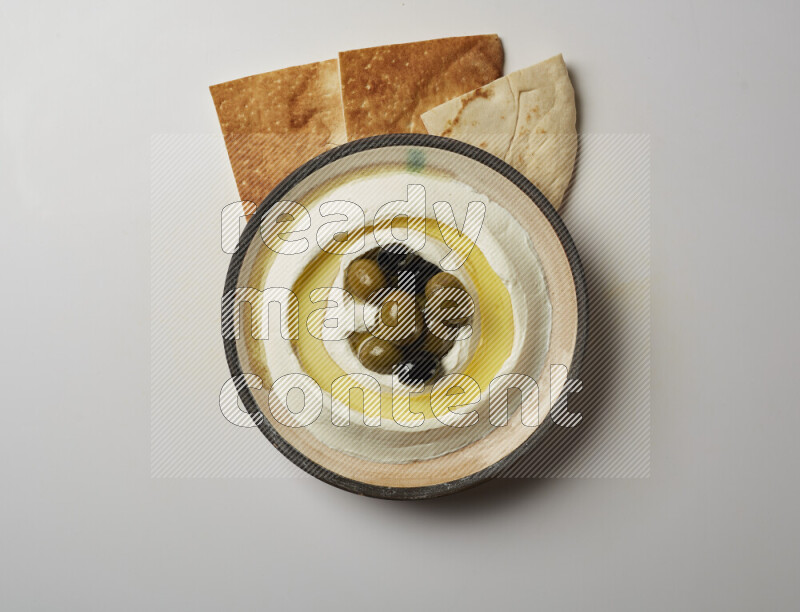 Lebnah garnished with whole black olives in a pottery plate on a white background