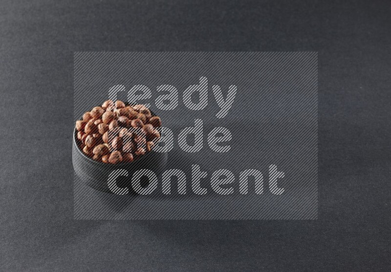 A black pottery bowl full of peeled hazelnuts on a black background in different angles