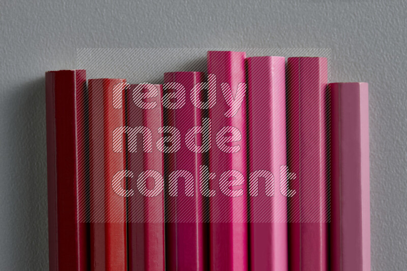 مجموعة من أقلام الرصاص الملونة مرتبة لتعرض تدرجا من اللون الوردي والأحمر علي خلفية رمادية