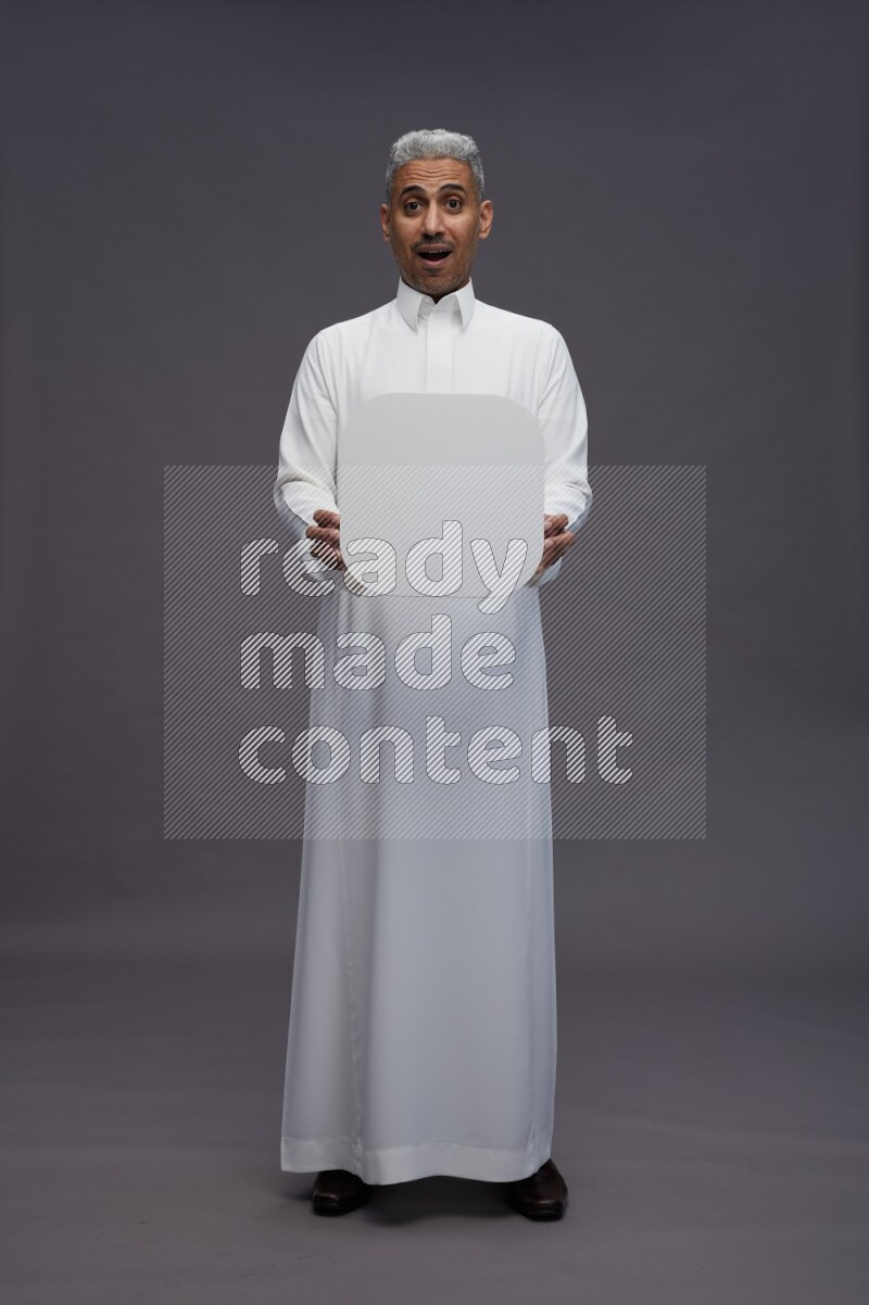 Saudi man wearing thob standing holding social media sign on gray background
