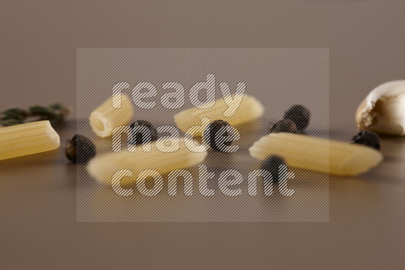 Raw pasta with different ingredients such as cherry tomatoes, garlic, onions, red chilis, black pepper, white pepper, bay laurel leaves, rosemary and cardamom on beige background