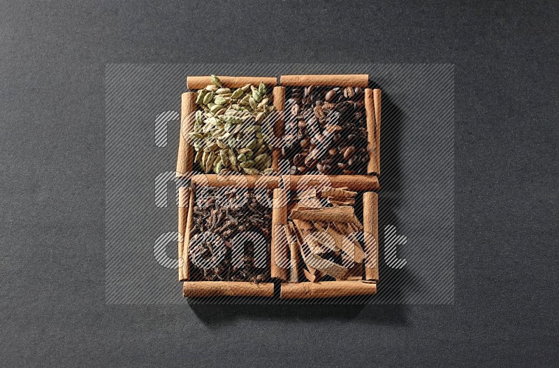 4 مربعات من عيدان القرفة ممتلئة بحبوب القهوة وقطع القرفة والقرنفل وحبوب الهيل على أرضية سوداء