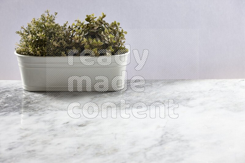 Multiple green artificial plants in white pot on grey marble background