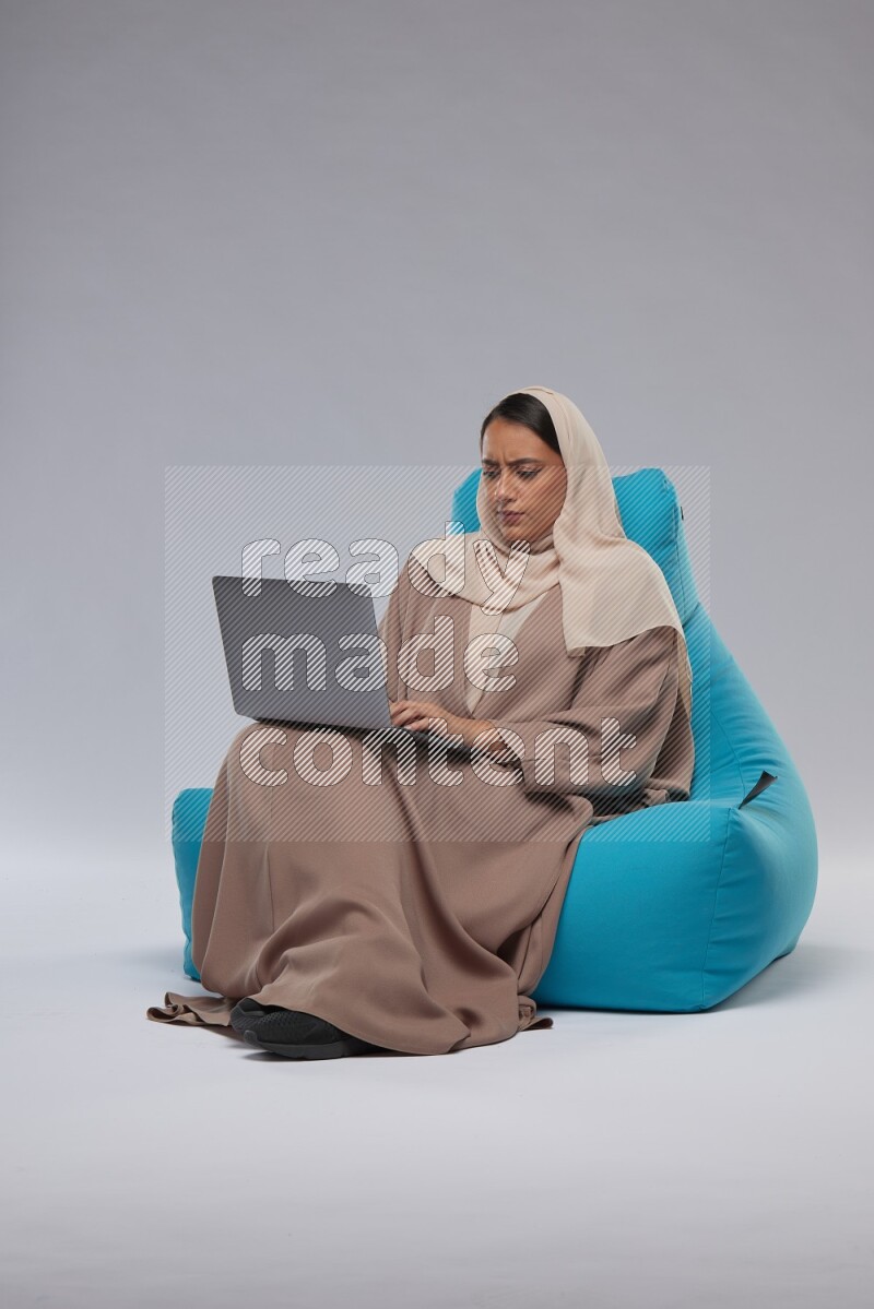A Saudi woman sitting on a blue beanbag and working on laptop