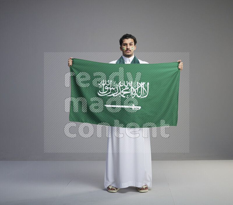 رجل سعودي يرتدي ثوب ابيض ويحمل علم السعودية