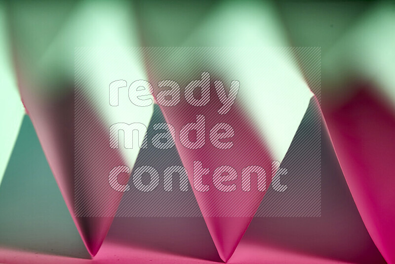 A close-up abstract image showing sharp geometric paper folds in green and pink gradients