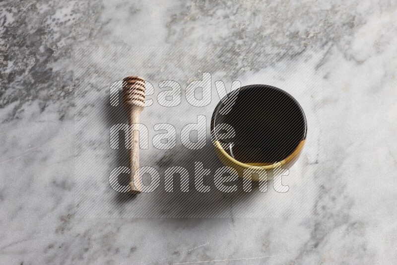 Multicolored pottery bowl with wooden honey dipper on the side on grey marble background
