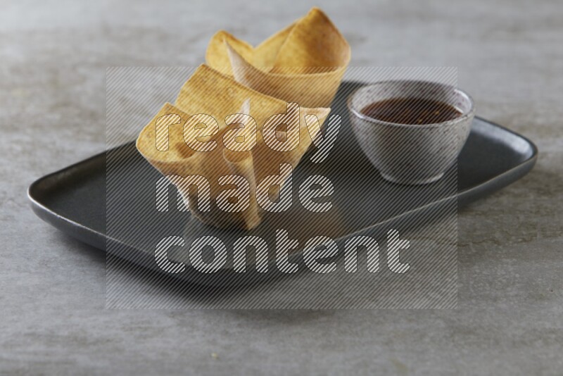 wonton cups with soy sauce ramkin on rectangle dark grey ceramic plate on grey textured counter top