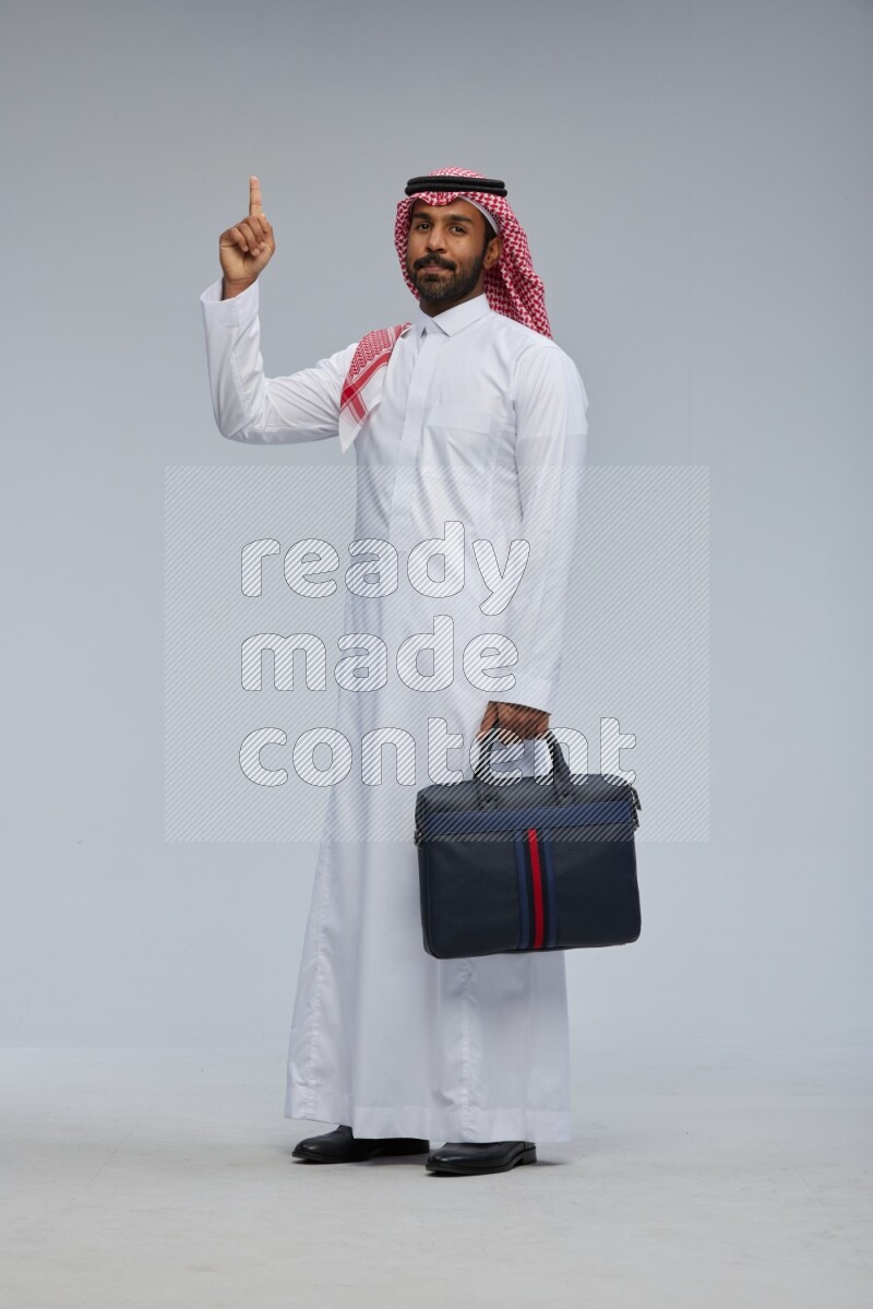 Saudi man Wearing Thob and shomag standing holding bag on Gray background