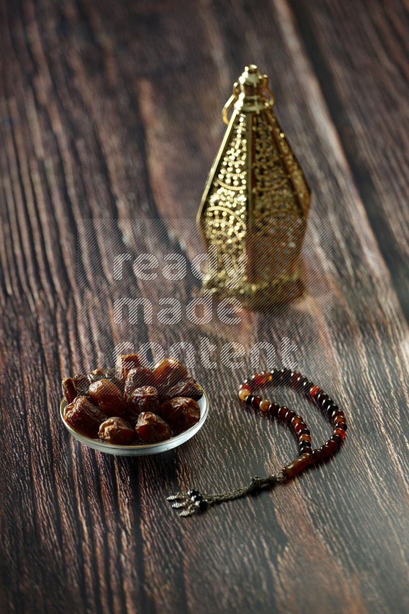 A golden lantern with different drinks, dates, nuts, prayer beads and quran on brown wooden background