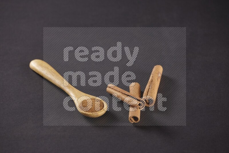 3 Cinnamon sticks stacked beside a wooden spoon full of cinnamon powder on black background in different angles
