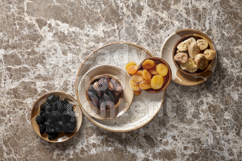 Dried fruits in pottery plates and wooden bowls in a light setup