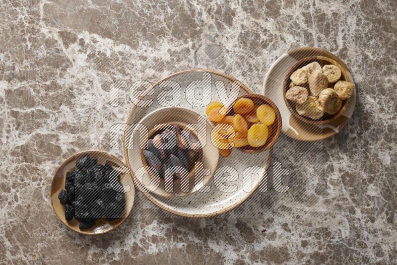 Dried fruits in pottery plates and wooden bowls in a light setup
