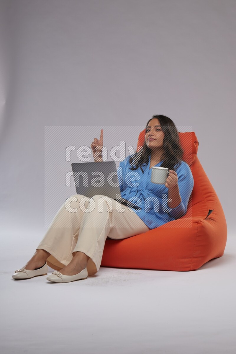 A woman sitting on an orange beanbag and working on laptop
