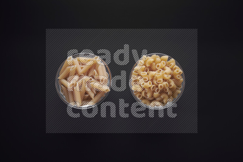 Different pasta types in glass bowls on black background