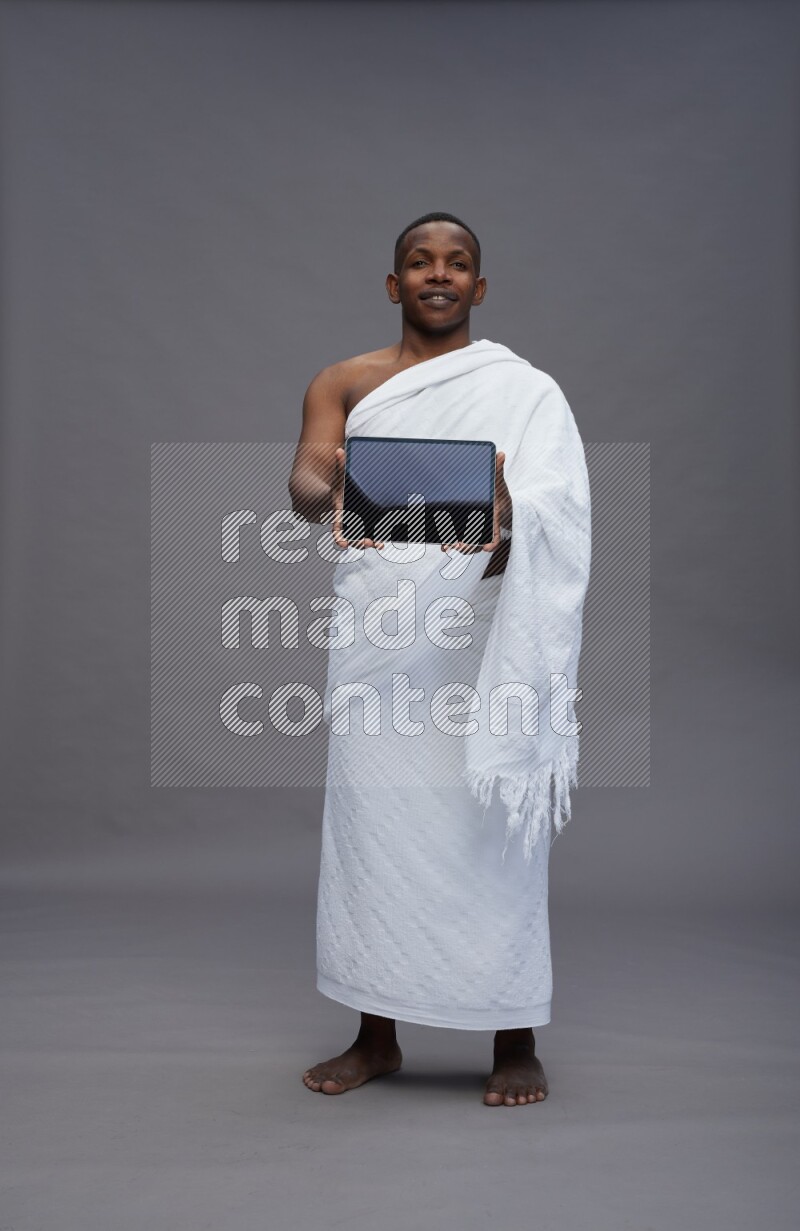 A man wearing Ehram Standing showing tablet to camera on gray background