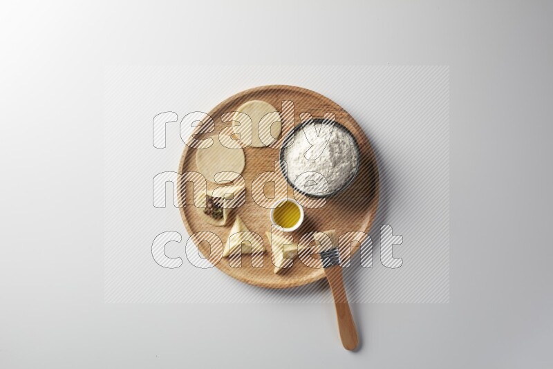two closed sambosas and one open sambosa filled with meat while flour, and oil with oil brush aside in a wooden dish on a white background